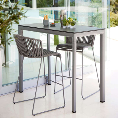 Moments Outdoor Bar Stool by Cane-Line, showing moments outdoor bar stools with table in live shot.