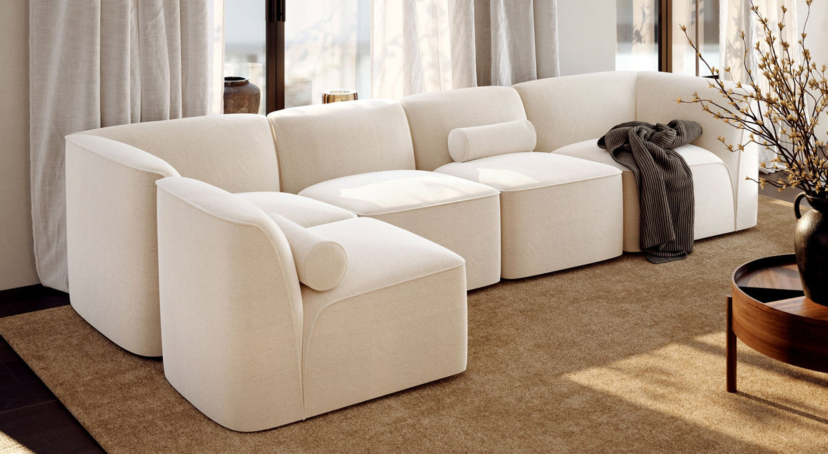 WOUD Flora modular sectional in cream bouclé with a walnut side table and wool rug in a sunlit modern living room