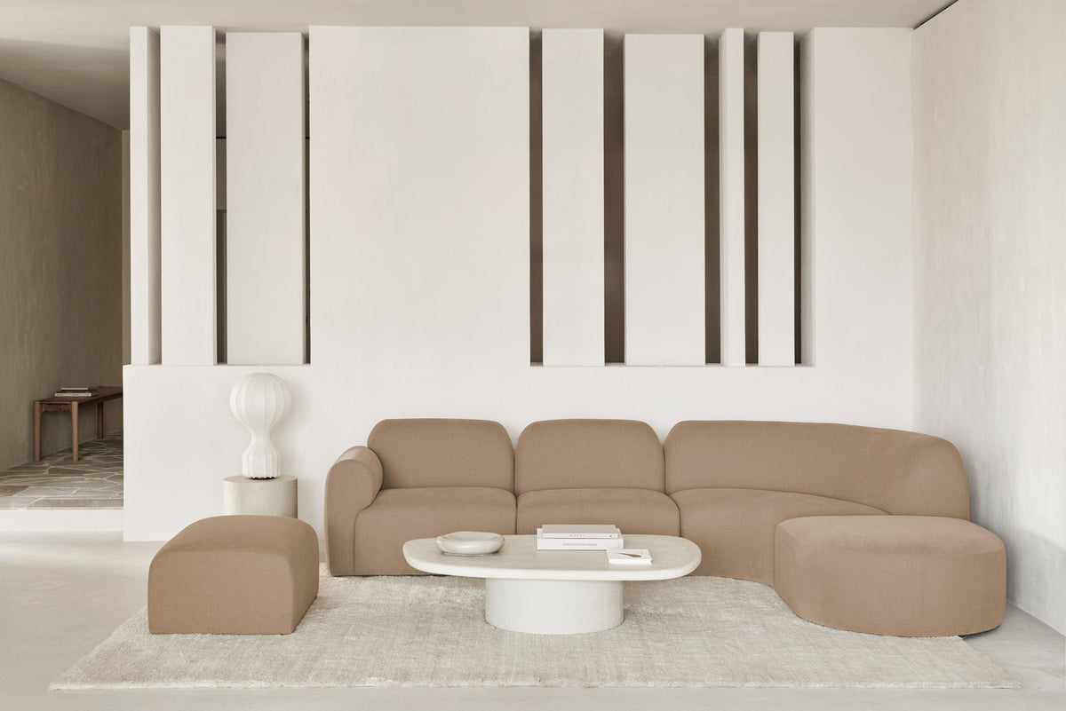 Ethnicraft Bulky curved sectional sofa in sand bouclé with matching ottoman, round coffee table and wool rug in a pale modern living room