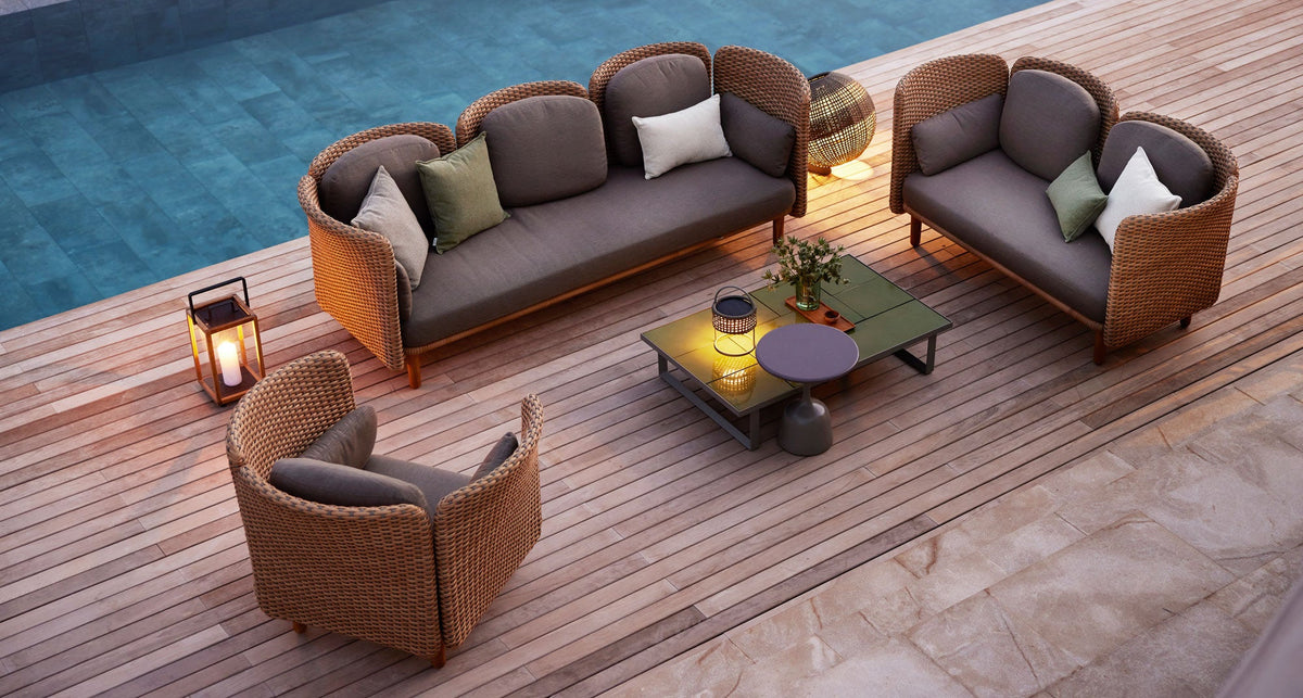 Cane-Line Arch outdoor lounge sofa with a fire table on a timber terrace at dusk