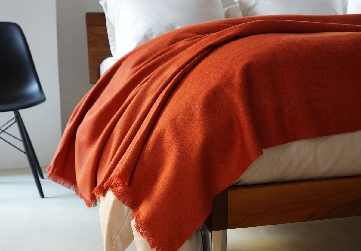 A rust lambswool throw with fringed edges draped across the foot of a modern wooden bed