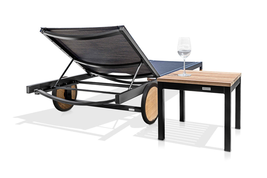 Ekka Teak Side Table by Mamagreen, showing back view of ekka teak side table in black sand aluminum/teak wood with sunlounger.