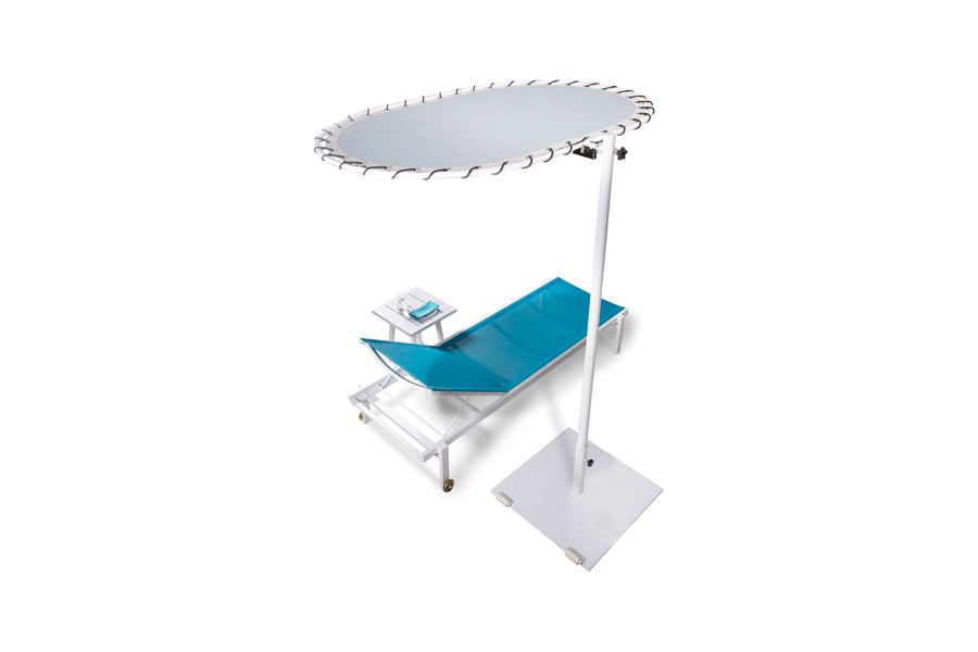 Sombrero Personal Medium Shade with Wheels by Mamagreen, showing angle view of sombrero personal medium shade with wheels in ink urban white galvanized steel/marble glacier blue sunbrella shade with table & sunlounger.