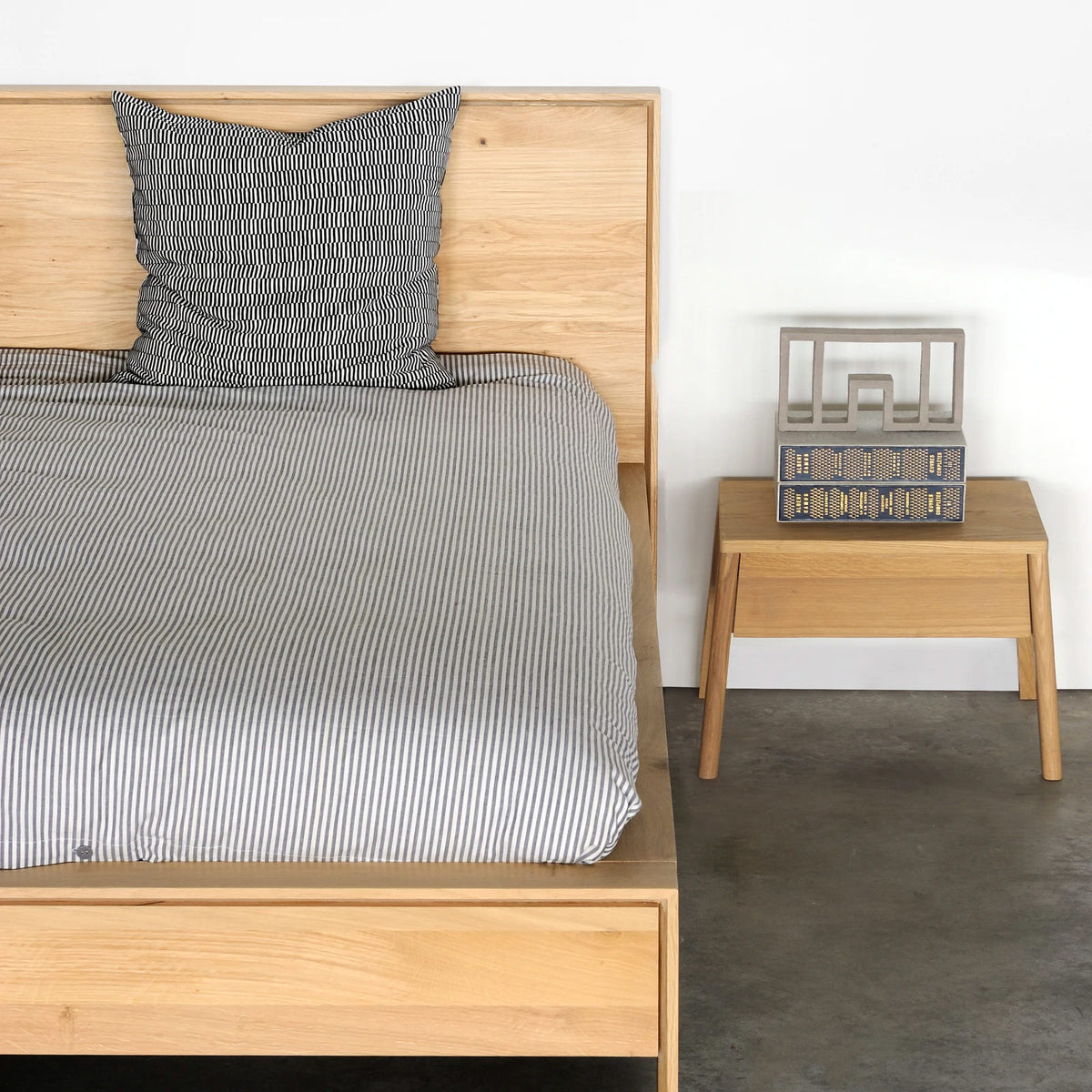 Air Oak Bedside Table by Ethnicraft, showing front view of bedside table with bed in the live shot.