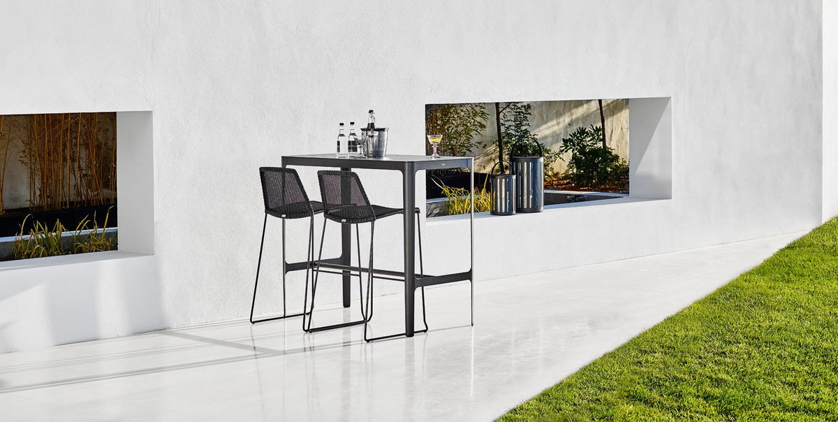 Breeze Stackable Bar Chair by Cane-Line, showing breeze stackable bar chairs with table in live shot.