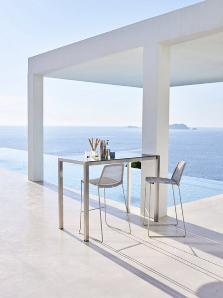 Breeze Stackable Bar Chair by Cane-Line, showing breeze stackable bar chairs with table in live shot.