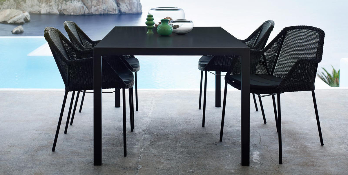 Breeze Stackable Dining Chair by Cane-Line, showing breeze stackable dining chairs with table in live shot.