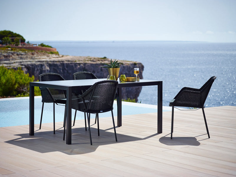 Breeze Stackable Dining Chair by Cane-Line, showing breeze stackable dining chairs with table in live shot.