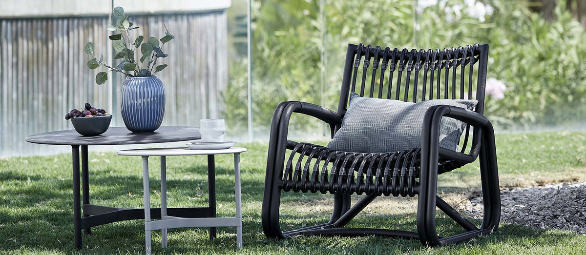 Curve Outdoor Lounge Chair by Cane-line, showing curve outdoor lounge chair with tables in live shot.
