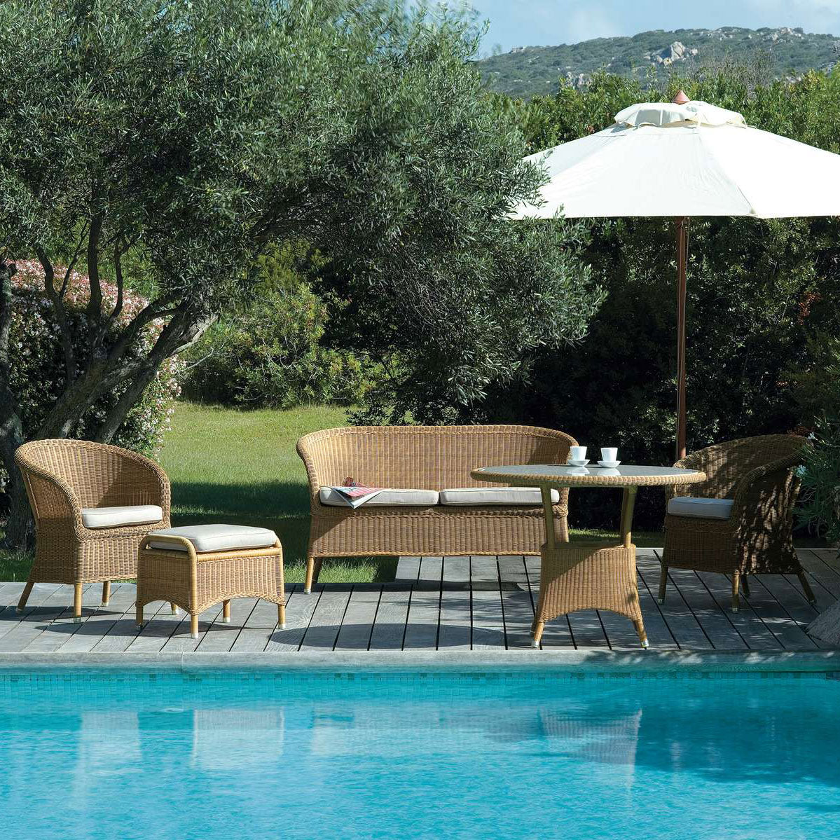 Derby Arm Chair by Cane-Line, showing derby arm chairs with table, sofa & footstool in live shot.
