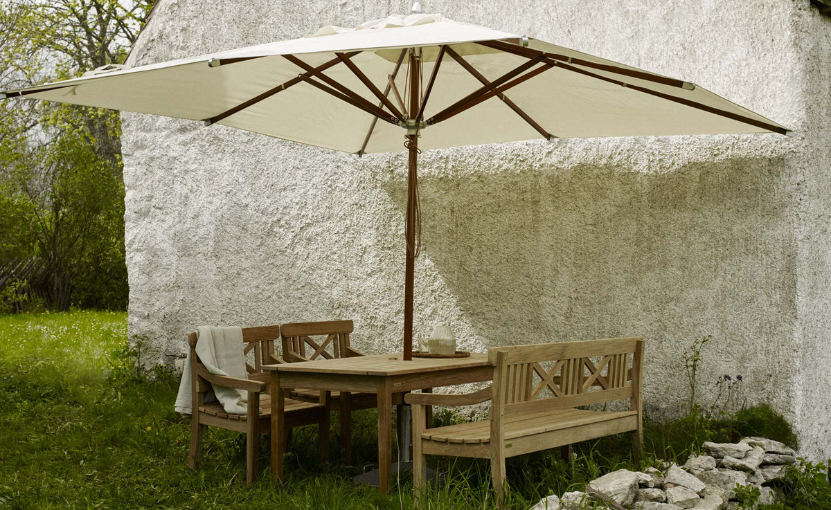 Drachmann Rectangle Teak Table by Skagerak, showing rectangle teak table with bench, chairs & umbrella in live shot.
