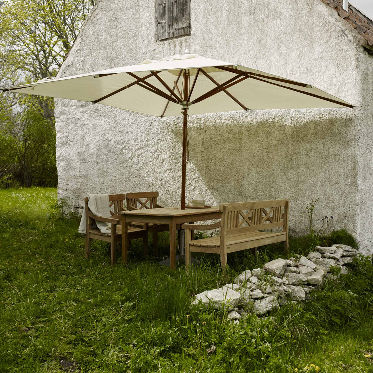 Drachmann Teak Chair by Skagerak, showing drachmann teak chairs with table, bench and umbrella in live shot.