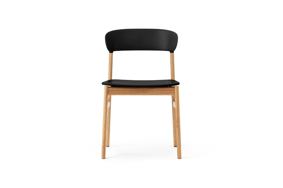 Herit Chair by Normann Copenhagen, showing front view of herit chair in oak wood legs/black plastic shell seat.