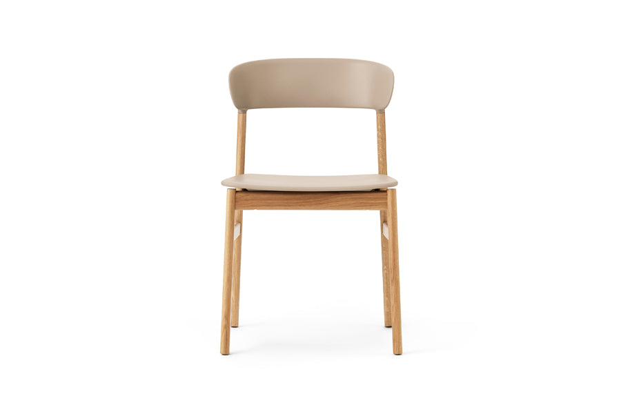 Herit Chair by Normann Copenhagen, showing front view of herit chair in oak wood legs/sand plastic shell seat.