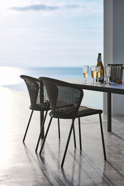 Lean Stackable Dining Chair by Cane-Line, showing lean stackable dining chairs with table in live shot.