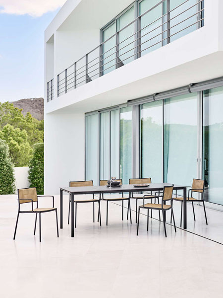 Less Stackable Dining Armchair by Cane-Line, showing less stackable dining armchairs with table in live shot.