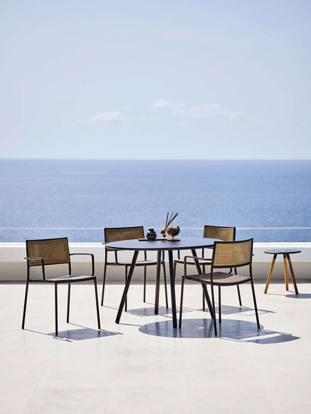 Less Stackable Dining Armchair by Cane-Line, showing less stackable dining armchairs with table in live shot.