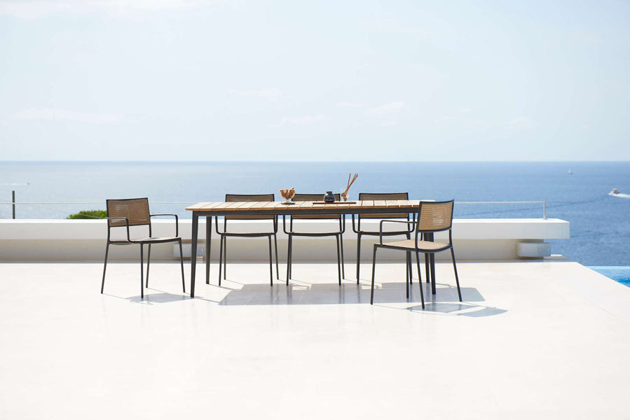 Less Stackable Dining Armchair by Cane-Line, showing less stackable dining armchairs with table in live shot.