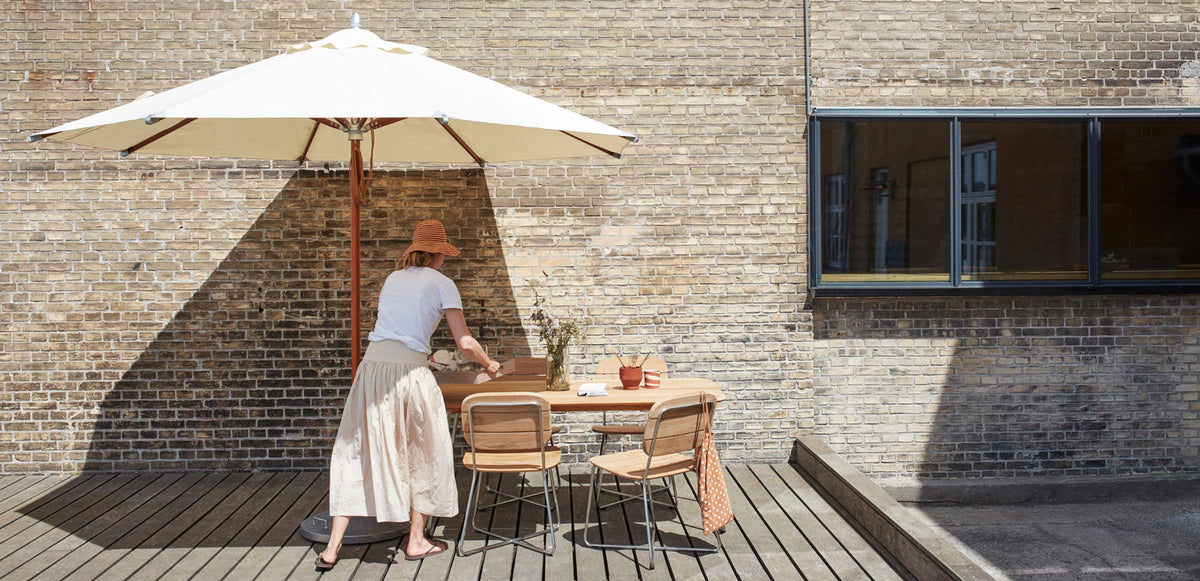 Lilium Teak Table by Skagerak, showing lilium teak table with chairs & umbrella in live shot.