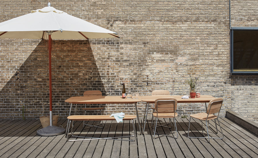 Lilium Teak Table by Skagerak, showing lilium teak table with bench, chairs & umbrella in live shot.