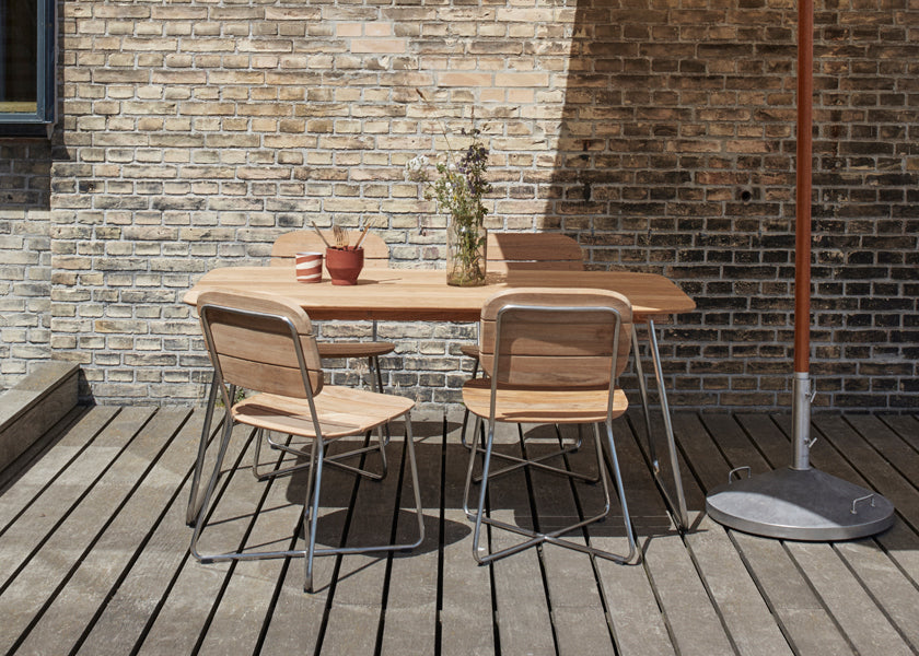 Lilium Teak Table by Skagerak, showing lilium teak table with chairs & umbrella in live shot.