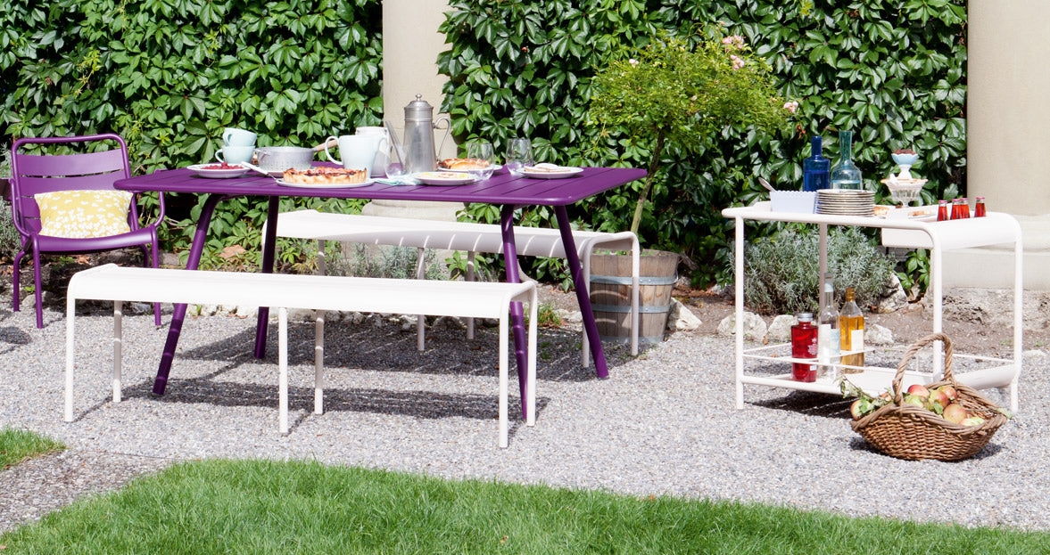 Luxembourg 3 Seater Bench w/o Back by Fermob, showing angle view of bench with table in the live shot.