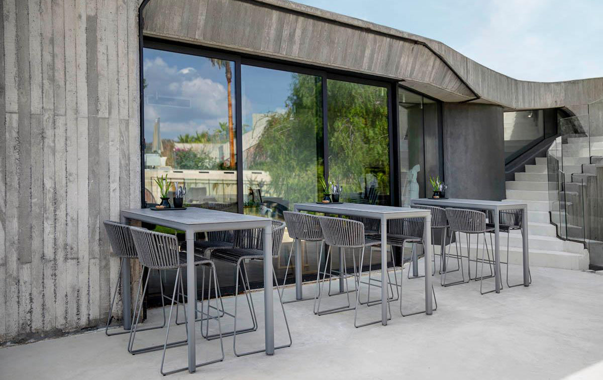 Moments Outdoor Bar Stool by Cane-Line, showing moments outdoor bar stools with tables in live shot.