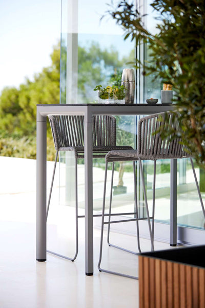 Moments Outdoor Bar Stool by Cane-Line, showing moments outdoor bar stools with table in live shot.
