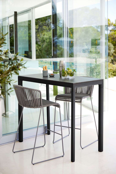 Moments Outdoor Bar Stool by Cane-Line, showing moments outdoor bar stools with table in live shot.