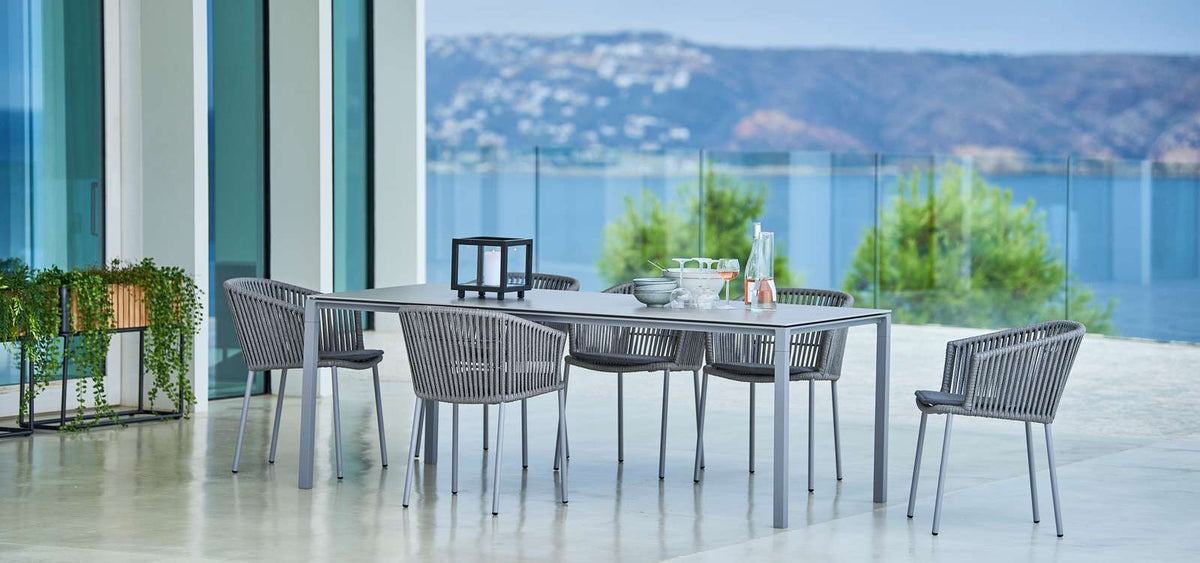 Moments Stackable Dining Armchair by Cane-Line, showing moments stackable dining armchairs with table in live shot.