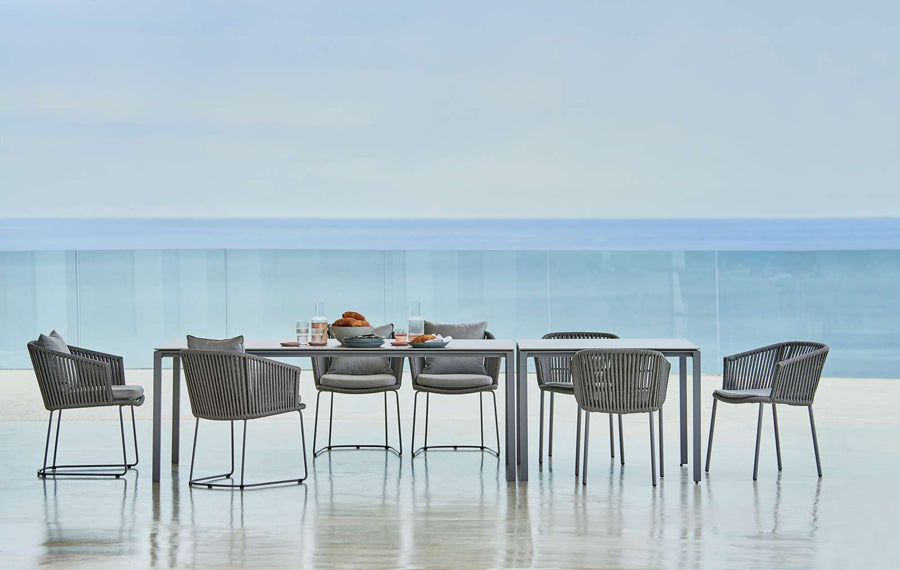 Moments Stackable Dining Armchair by Cane-Line, showing moments stackable dining armchairs with table & chairs in live shot.