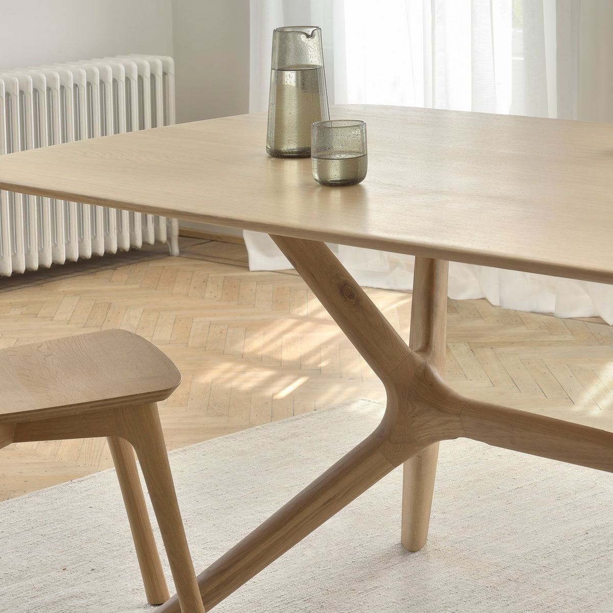 X Dining Table by Ethnicraft, showing closeup view of oak x dining table with chair in live shot.