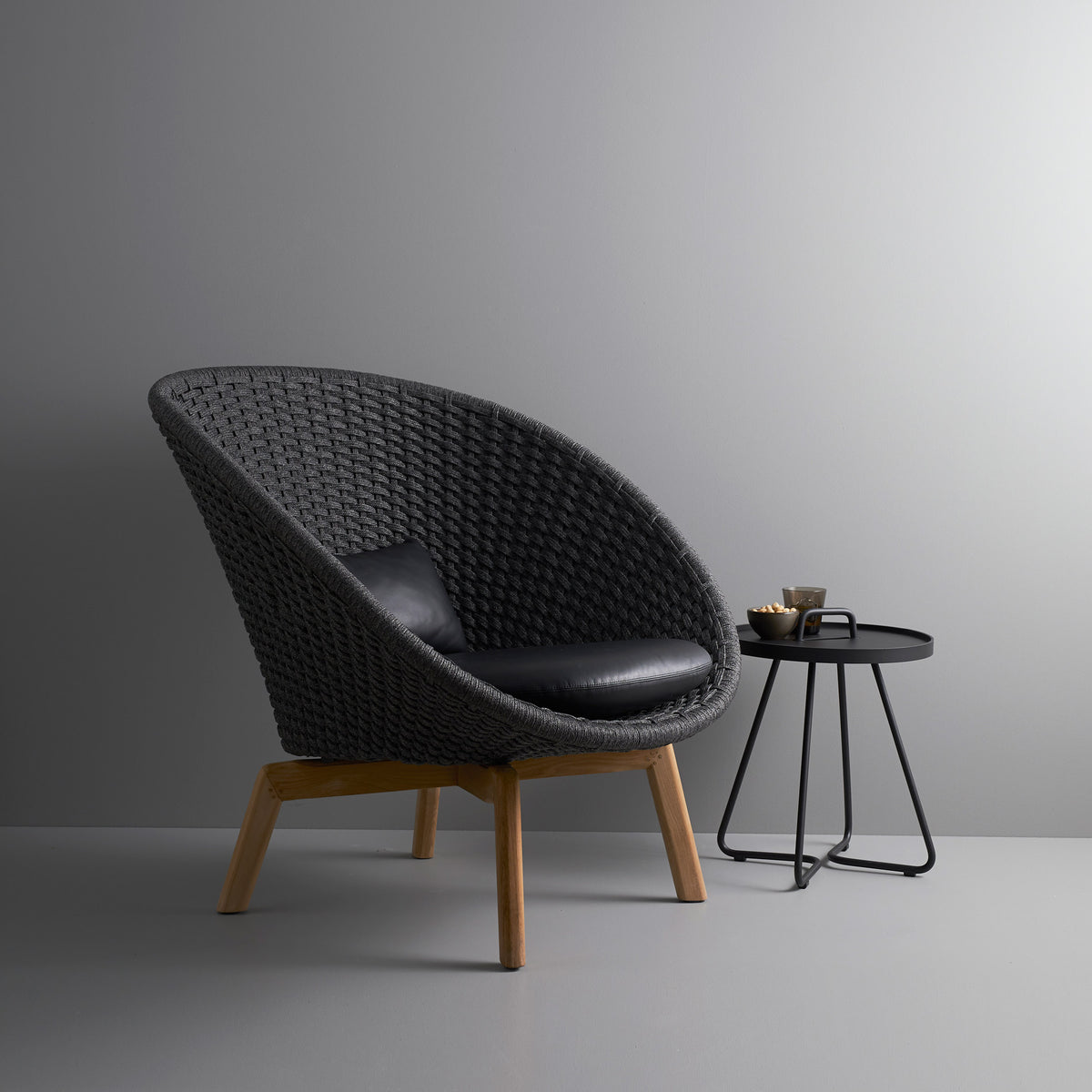 Peacock Indoor Lounge Chair by Cane-Line, showing peacock indoor lounge chair with table in live shot.