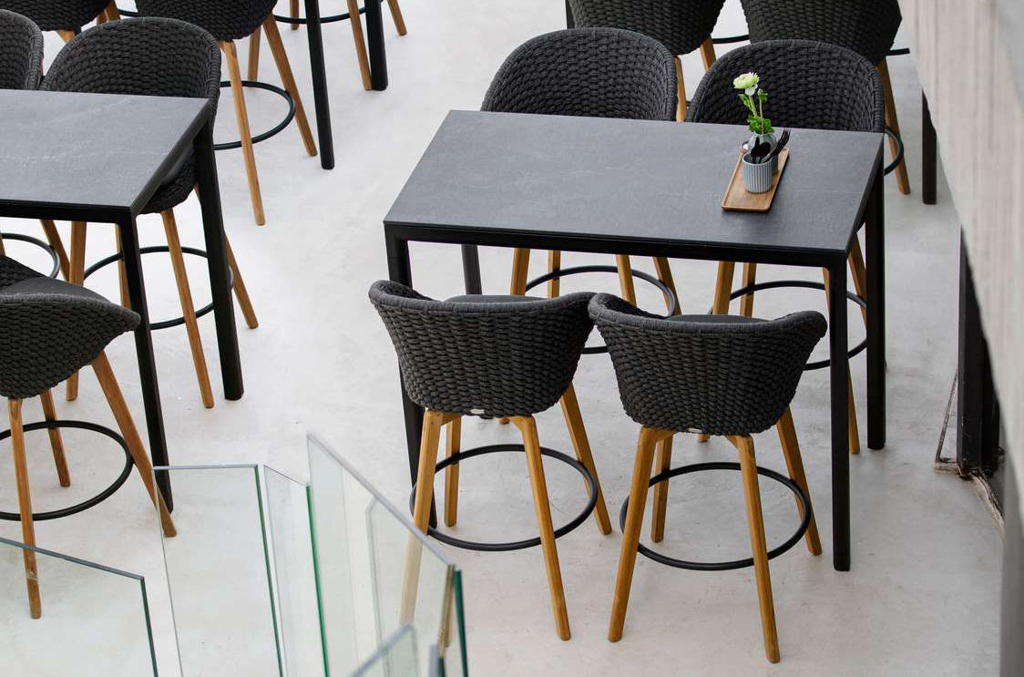 Peacock Outdoor Bar Chair with Teak Legs by Cane-Line, showing peacock outdoor bar chairs with tables in live shot.