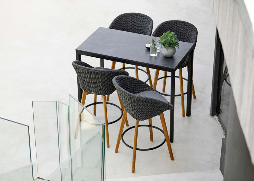 Peacock Outdoor Bar Chair with Teak Legs by Cane-Line, showing peacock outdoor bar chairs with table in live shot.