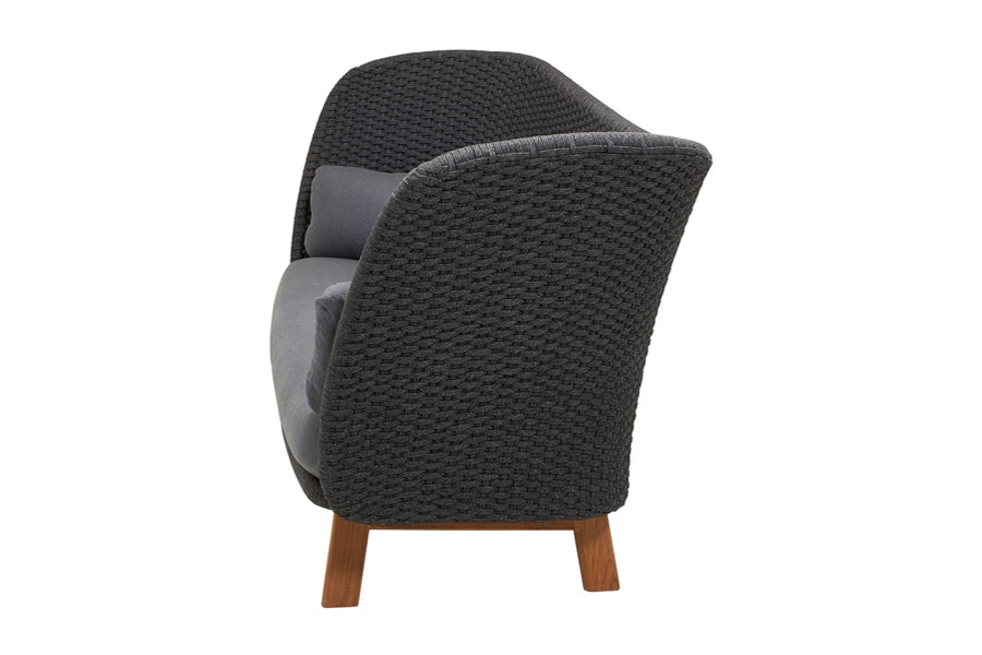Peacock Wing 3 Seater Sofa with Teak Legs by Cane-Line, showing side view of peacock wing 3 seater sofa with teak legs in dark grey soft rope/grey natte cushions.