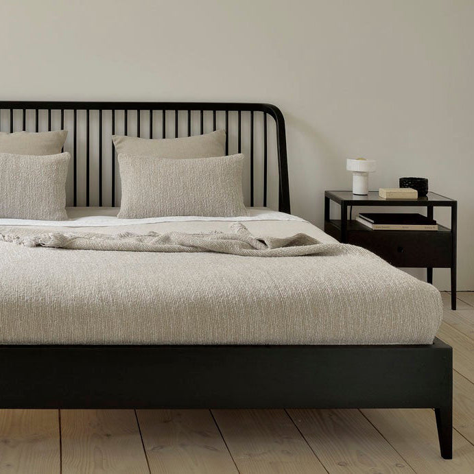 Spindle Bedside Table by Ethnicraft, showing closeup view of spindle bedside table with bed in live shot.