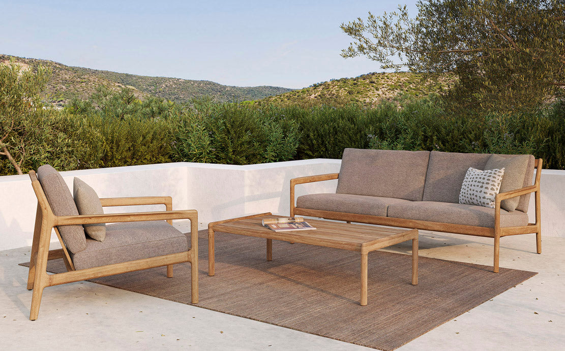 Jack Outdoor Coffee Table by Ethnicraft , showing front view of teak outdoor coffee table with sofa in live shot.