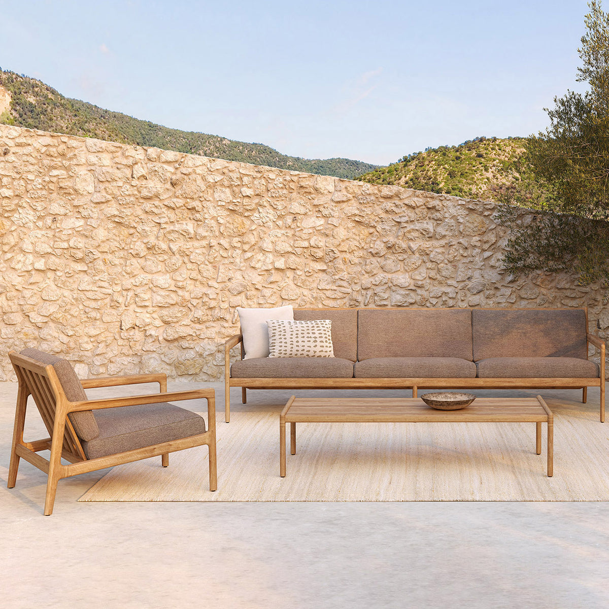 Jack Outdoor Coffee Table by Ethnicraft , showing front view of teak outdoor coffee table with sofa in live shot.
