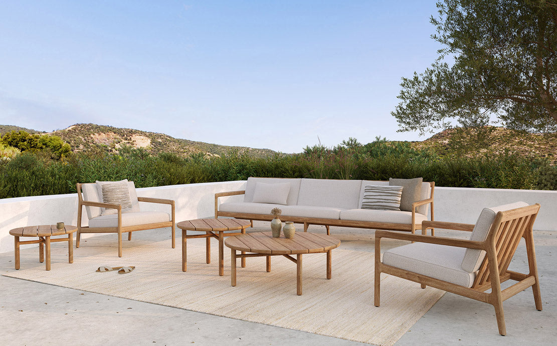 Quatro Outdoor Side Table by Ethnicraft, showing front view of teak side table with sofa in live shot.