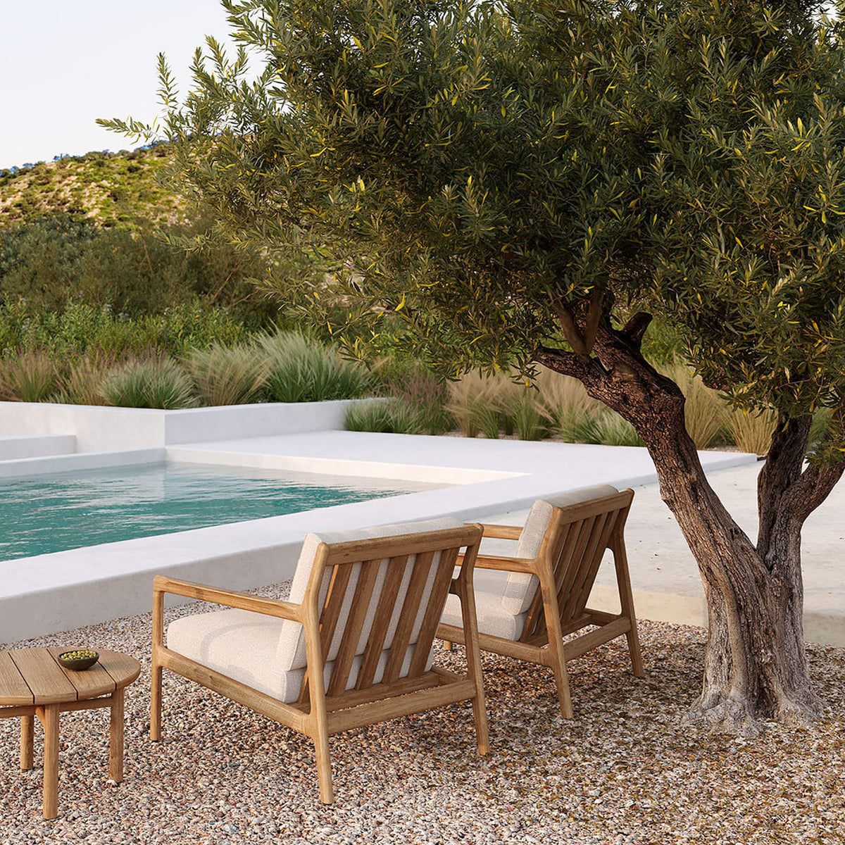 Quatro Outdoor Side Table by Ethnicraft, showing front view of teak side table with sofa in live shot.